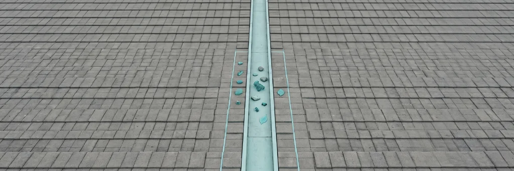A wide field of dense grey geometric tiles extending across the frame, with a single narrow vertical channel of teal cutting through the centre.